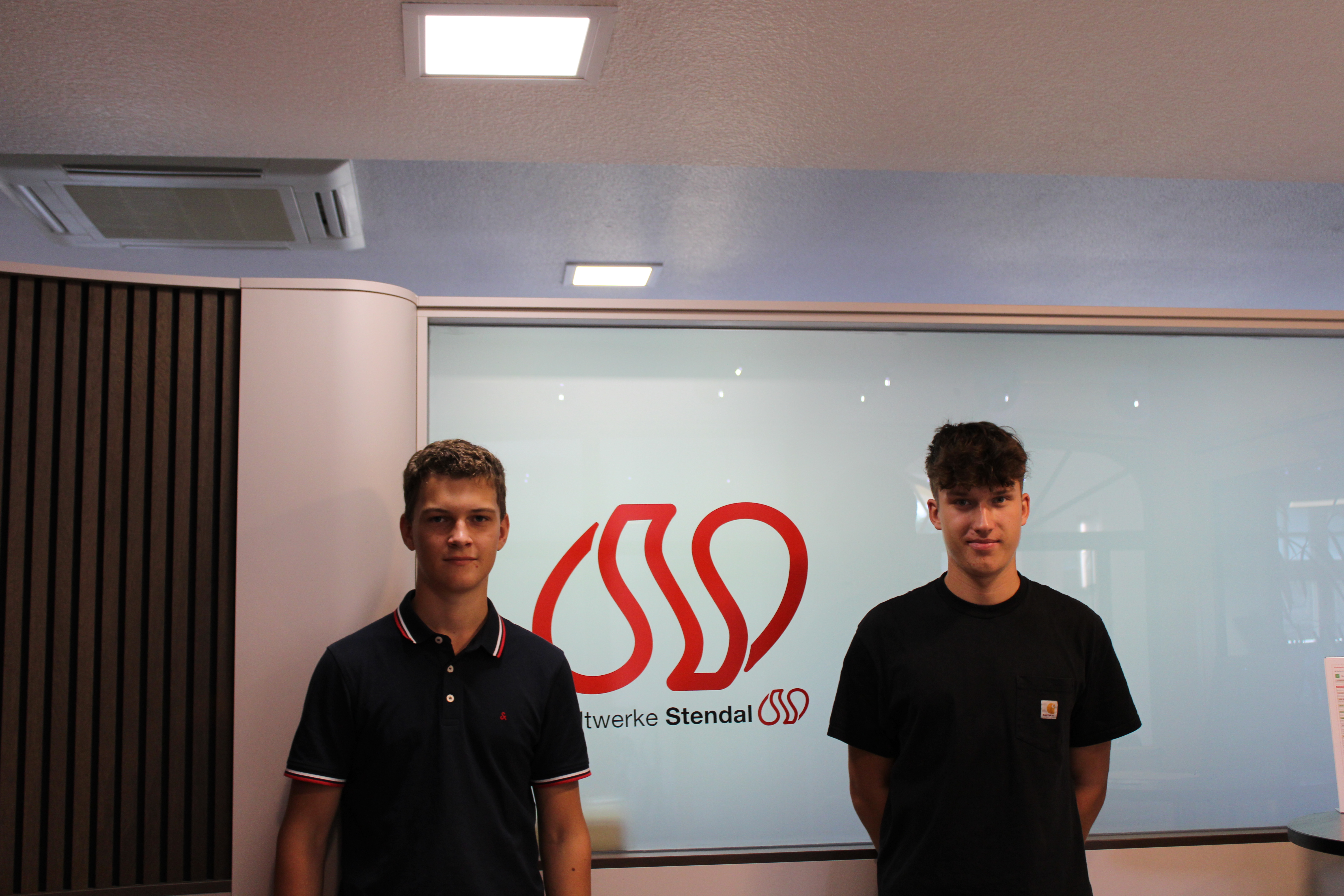 unsere neuen Azubis Julian Nahrstedt und Felix Luttkus vor dem Stadtwerke Stendal Logo im Kundencenter