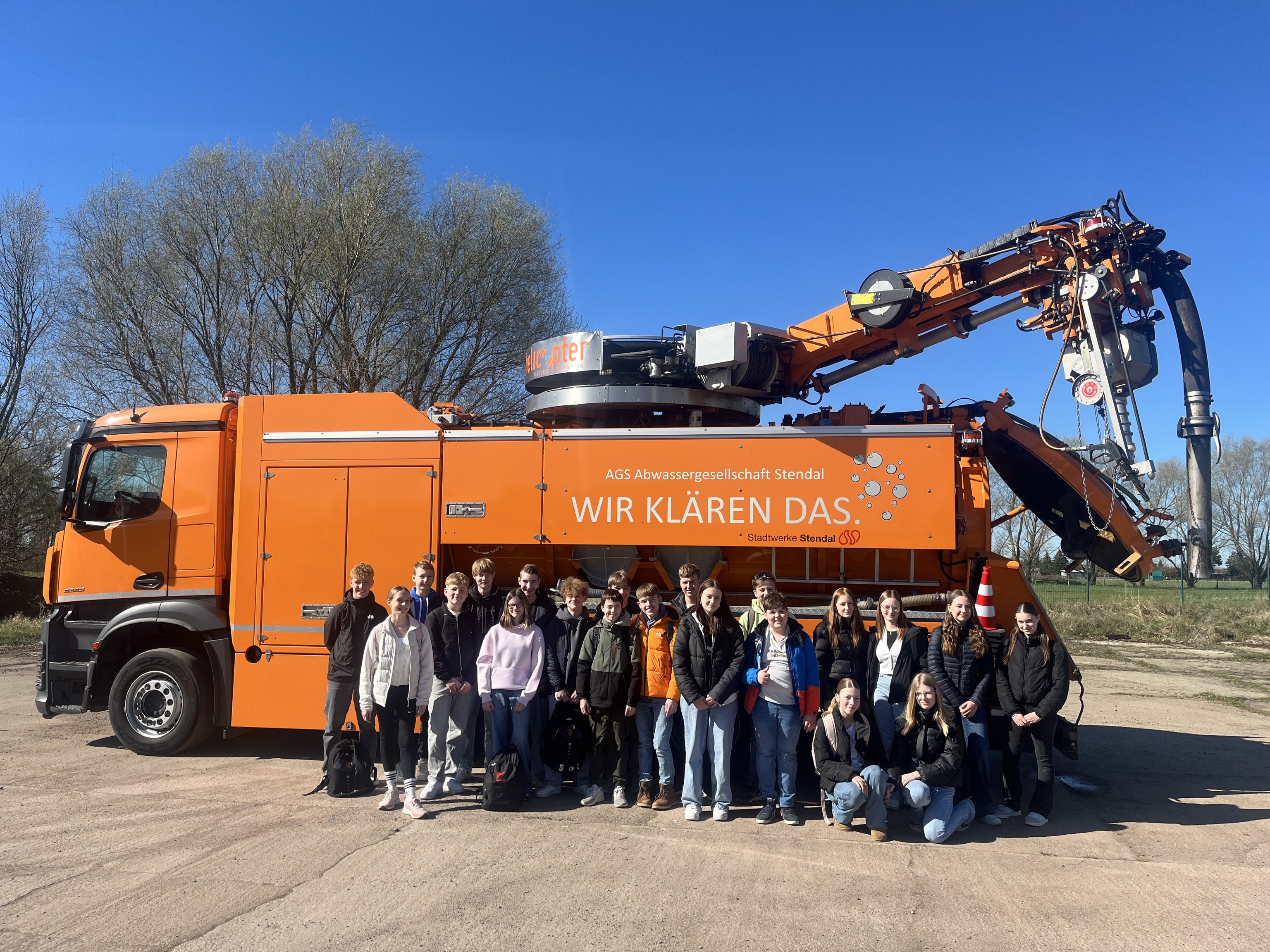 Schulklasse vor dem orangefarbenen Saugspülwagen beim Zukunftstag 2025